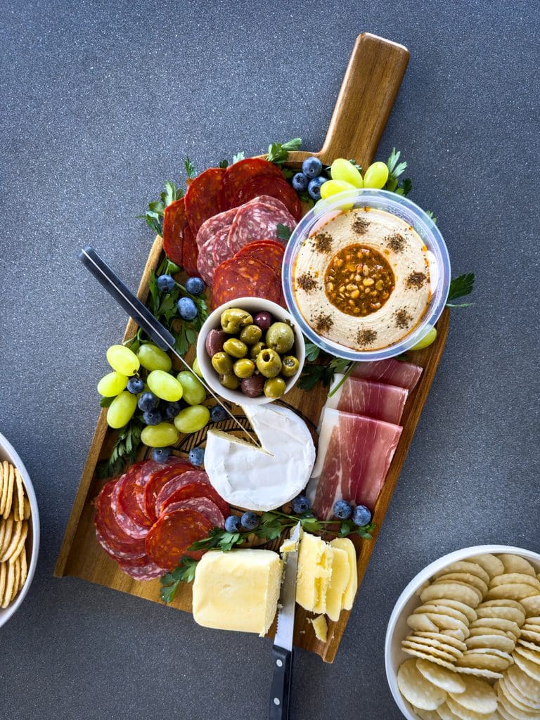 Top view of a gourmet charcuterie board or cheese platter with various meats, fruits and cheese on a wooden board